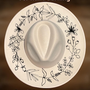 May include: A cream-coloured fedora hat featuring a black floral design around the brim. The text "For Hand Burning" and "CoolMoonDesigns" are printed on the hat.