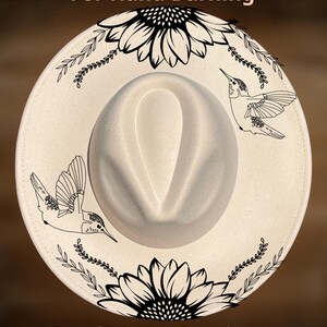 May include: Cream-coloured fedora hat with a wide brim, featuring black line art of sunflowers and hummingbirds. The text "For Hand Burning" and "CoolMoonDesigns" are printed on the hat.