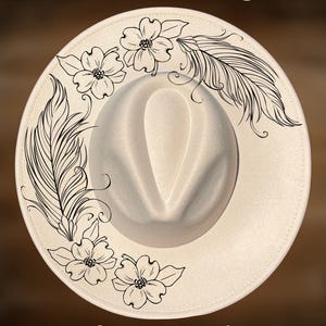 May include: Cream-colored fedora hat with hand-burned floral and feather designs. The hat features a wide brim and a pinched crown. The text "For Hand Burning" and "CoolMoonDesigns" are visible on the hat.