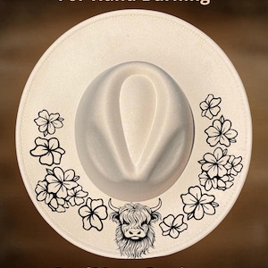 May include: A cream-coloured wide-brim hat featuring a black line-art illustration of a Highland cow centred at the bottom, flanked by floral patterns on both sides. The text "For Hand Burning" appears at the top and "CoolMoonDesigns" at the bottom.