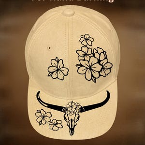 May include: A beige baseball cap with a black floral and bull skull design. The cap features the text "For Hand Burning" and "CoolMoonDesigns". The design includes a bull skull with flowers and additional floral accents.