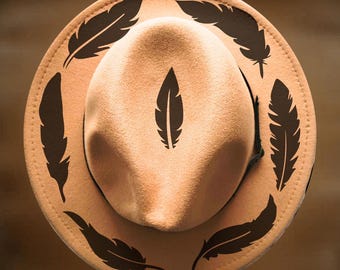 May include: A tan felt hat featuring dark brown feather designs printed on the crown and brim. The text "For Hand Burning" appears at the top, and "CoolMoonDesigns" is printed at the bottom. The hat has a structured crown and wide brim.