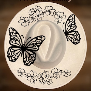 May include: A white fedora hat with black butterfly and floral designs. The hat features the text "For Hand Burning" and "CoolMoonDesigns". The hat is a stylish accessory.
