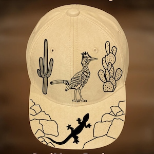 Può includere: Un cappellino da baseball beige con grafica nera a tema deserto. Il design include un cactus, un roadrunner e una lucertola, con il testo "For Hand Burning" e "CoolMoonDesigns".