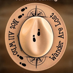 May include: Tan fedora hat with a black brim, featuring a compass design and the text "Not All Who Wander Are Lost." The hat also includes the text "For Hand Burning" and "CoolMoonDesigns."