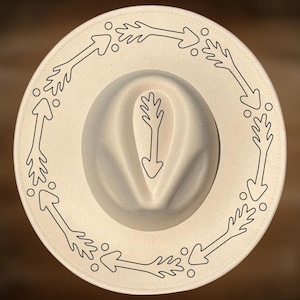 May include: Cream-colored hat with a wide brim and a central indentation. The brim is adorned with a repeating pattern of black arrows pointing counter-clockwise. An arrow design is also centered on the crown of the hat.