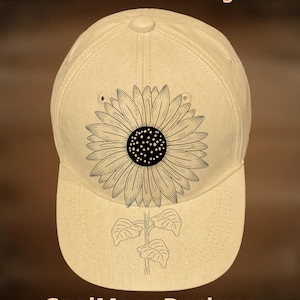 May include: A beige baseball cap with a black sunflower design. The cap has a curved brim and a button on top. The text "For Hand Burning" and "CoolMoonDesigns" are printed on the cap.