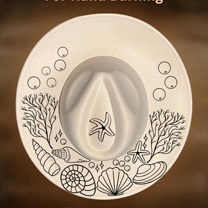 May include: A cream-coloured fedora hat with a wide brim, featuring black line art of seashells, starfish, and coral. The text "For Hand Burning" and "CoolMoonDesigns" are printed on the hat.