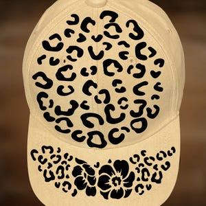 May include: A beige baseball cap featuring a black leopard print pattern on the front and brim. The leopard print consists of black spots of different sizes. The brim also has a floral design.