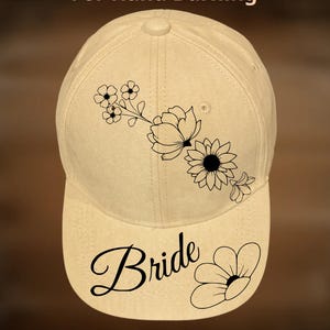 May include: A beige baseball cap featuring a black line art floral design on the crown and the word Bride with a small flower graphic on the brim. The text For Hand Burning appears above the cap and CoolMoonDesigns appears below the cap.