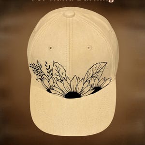 May include: A beige baseball cap with a black sunflower and leaf design on the front. The text "For Hand Burning" is above the cap, and "CoolMoonDesigns" is below.