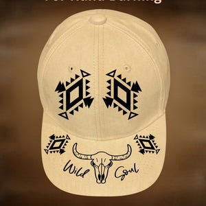 May include: A beige baseball cap with black geometric designs and the text "Wild Soul" and a bull skull graphic on the front. The text "For Hand Burning" and "CoolMoonDesigns" are also visible.