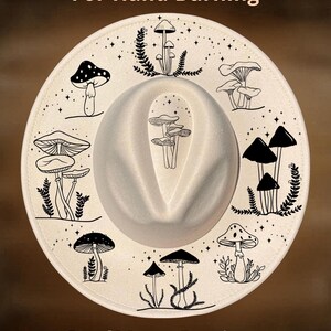May include: A white fedora hat with a wide brim, decorated with a hand-burned design of mushrooms and foliage. The hat has the text "For Hand Burning" and "CoolMoonDesigns" printed on it.