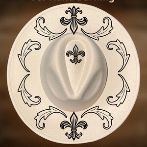 May include: A cream-colored fedora hat with black decorative flourishes and a fleur-de-lis design. The hat has the text "For Hand Burning" and "CoolMoonDesigns" printed on it. The hat is a stylish accessory.