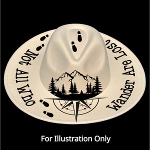 May include: A cream-colored fedora hat with a black mountain and compass design. The hat features the text "Not All Who Wander Are Lost" around the brim and footprints. The hat is a stylish accessory for outdoor enthusiasts.