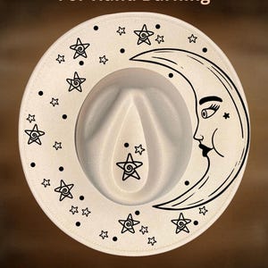 May include: A cream-coloured fedora hat with a wide brim, featuring a black crescent moon and star design. The hat has the text "For Hand Burning" and "CoolMoonDesigns" printed on it.