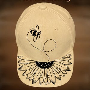 May include: Tan baseball cap with a black bee and sunflower design. The cap features the text "For Hand Burning" and "CoolMoonDesigns". The bee is above the brim, with a dotted line trailing behind it.