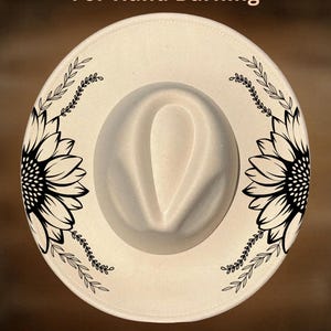 May include: A cream-coloured fedora hat with a wide brim, decorated with a black sunflower design and leaf accents. The text "For Hand Burning" and "CoolMoonDesigns" are visible on the hat.