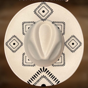 Op de afbeelding: Een crèmekleurige fedora hoed met een brede rand, met een geometrisch zwart patroon. De hoed heeft een ronde kroon en is voorzien van de tekst "For Hand Burning" en "CoolMoonDesigns".
