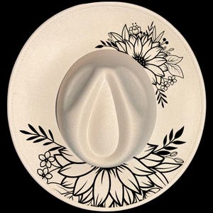 Puede incluir: Sombrero fedora color crema con ala ancha, adornado con un dise&ntilde;o floral negro. El sombrero presenta una corona cl&aacute;sica en forma de l&aacute;grima y un patr&oacute;n floral negro decorativo en el ala, adecuado para diversas ocasiones.