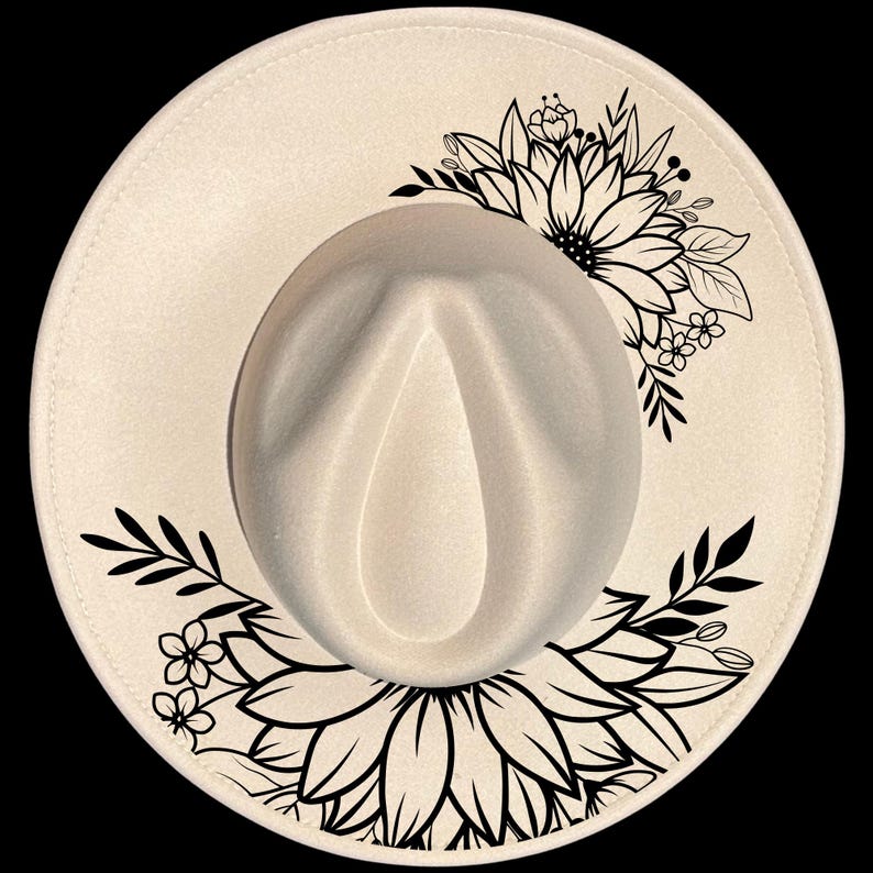 Puede incluir: Sombrero fedora color crema con ala ancha, adornado con un dise&ntilde;o floral negro. El sombrero presenta una corona cl&aacute;sica en forma de l&aacute;grima y un patr&oacute;n floral negro decorativo en el ala, adecuado para diversas ocasiones.