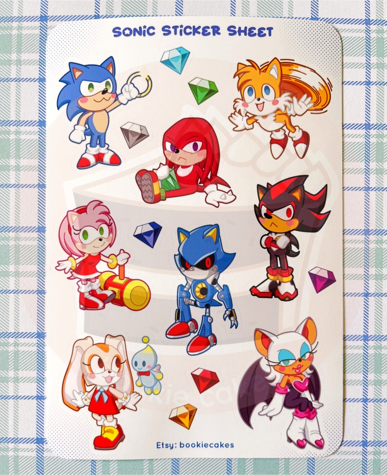 May include: A sticker sheet featuring characters from the Sonic the Hedgehog video game series. The sheet includes Sonic, Tails, Knuckles, Shadow, Metal Sonic, Amy Rose, Cream the Rabbit, and Rouge the Bat. The characters are depicted in a cartoon style and are surrounded by colorful gems.