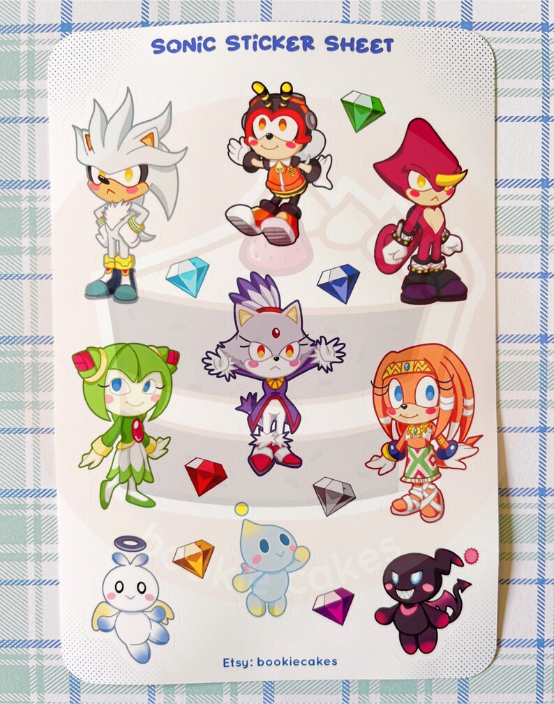 May include: A sticker sheet featuring characters from the Sonic the Hedgehog franchise. The sheet includes Sonic, Tails, Knuckles, Amy, Shadow, Rouge, Blaze, and Cream. The characters are depicted in a chibi style and are surrounded by colorful gems.