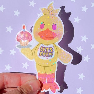 Pu&ograve; includere: Un pollo di cartone animato giallo glitterato con un cupcake rosa in mano. Il pollo indossa una maglietta gialla con la scritta "Let's Eat!" sullo sfondo. Lo sfondo &egrave; viola chiaro con stelle bianche.