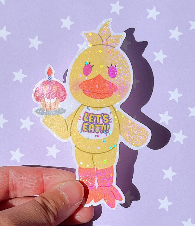 Pu&ograve; includere: Un pollo di cartone animato giallo glitterato con un cupcake rosa in mano. Il pollo indossa una maglietta gialla con la scritta "Let's Eat!" sullo sfondo. Lo sfondo &egrave; viola chiaro con stelle bianche.