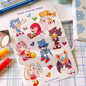 May include: A sticker sheet featuring characters from the Sonic the Hedgehog video game series. The sheet includes Sonic, Tails, Knuckles, Shadow, Metal Sonic, Amy Rose, Rouge the Bat, and Cream the Rabbit. The characters are depicted in a cartoon style and are surrounded by colorful gems.