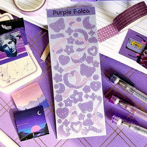May include: A sheet of purple and pink holographic stickers with a variety of shapes, including stars, moons, hearts, and ribbons. The sheet is labeled "Purple Polco".