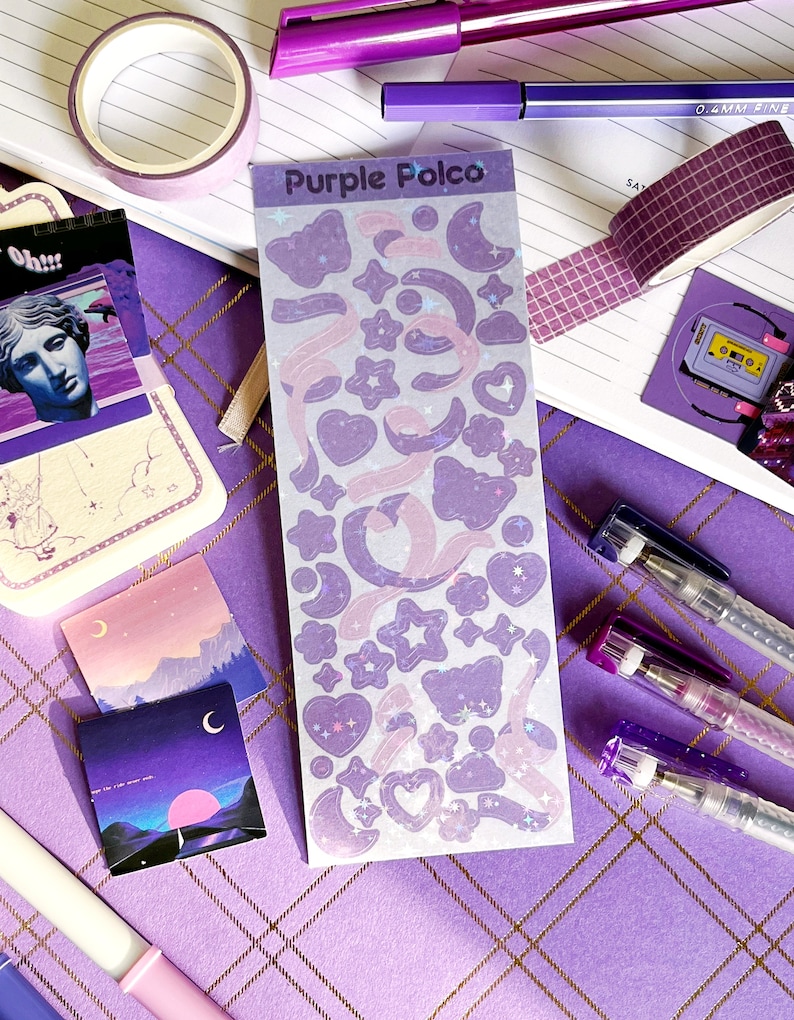 May include: A sheet of purple and pink holographic stickers with a variety of shapes, including stars, moons, hearts, and ribbons. The sheet is labeled "Purple Polco".