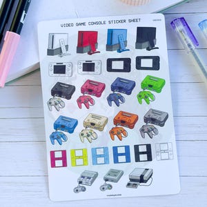 May include: A sticker sheet titled VIDEO GAME CONSOLE STICKER SHEET featuring various illustrated video game consoles and handheld devices in multiple colors, including white, red, blue, black, pink, green, orange, and gray, with controllers.