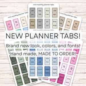 May include: A collection of adhesive mini monthly planner tabs arranged on multiple white sticker sheets. The tabs feature various pastel and muted color palettes, including pink, blue, green, and neutral tones, with printed month names and labels.
