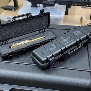 May include: Black hard cases with a gold pen inside one, and two closed cases with the letters "J" and "R" on them. The pen is engraved with the name "RAMIREZ". The cases are on a larger black case.