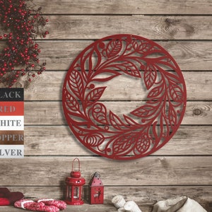 May include: Red metal wall decor in the shape of a wreath with a floral design. The wreath is hanging on a wooden wall with a rustic feel.