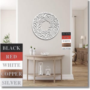 May include: White metal wall decor with a circular design featuring intricate floral patterns. The decor is shown hanging on a white wall in a living room setting.