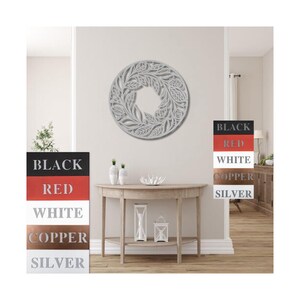 May include: A white, round, decorative wall hanging with a floral design. The wall hanging is mounted on a white wall in a room with a wooden floor. The wall hanging is available in black, red, white, copper, and silver.