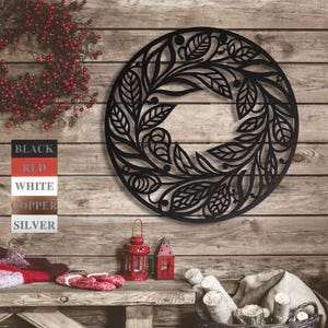 May include: Black metal wreath with a floral design. The wreath is round and has a delicate, intricate pattern of leaves and flowers. It is hanging on a wooden wall.