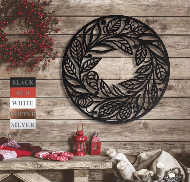 May include: Black metal wreath with a floral design. The wreath is round and has a delicate, intricate pattern of leaves and flowers. It is hanging on a wooden wall.