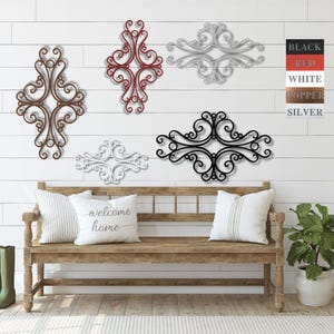 May include: Five decorative metal wall decor pieces in various styles and sizes. The pieces are in black, white, red, copper, and silver. The decor is displayed on a white wall with a wooden bench in front of it.