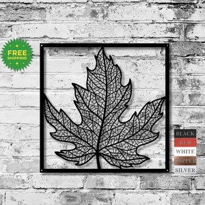 May include: Black metal leaf wall art. The leaf is intricately detailed with a network of veins and is set within a square black frame. The background is a white brick wall. The image also includes a green "FREE SHIPPING" sticker and color options.