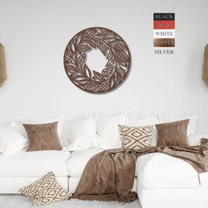 May include: A circular wall decoration featuring a floral design. The design is crafted from metal and has a brown finish. The decoration is hanging on a white wall above a white sofa with brown throw cushions and a brown blanket.