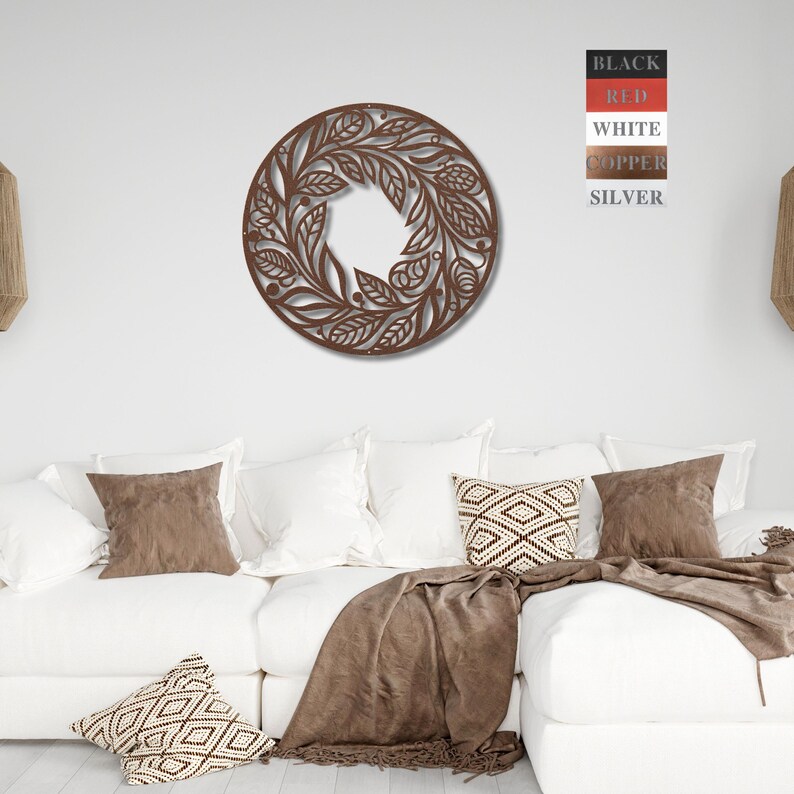 May include: A circular wall decoration featuring a floral design. The design is crafted from metal and has a brown finish. The decoration is hanging on a white wall above a white sofa with brown throw cushions and a brown blanket.