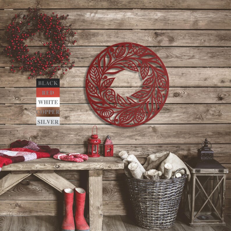 May include: Red metal wall decor in the shape of a wreath with a floral design. The wreath is hanging on a wooden wall with a rustic feel.