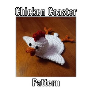 May include: A white crochet chicken coaster with a red comb, orange beak, and orange feet. The coaster has black eyes and is lying on a wooden surface. The text "Chicken Coaster Pattern" is displayed above and below the coaster.
