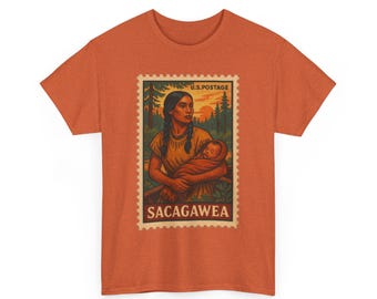 May include: Orange t-shirt featuring a vintage-style postage stamp design. The stamp depicts Sacagawea holding an infant, with the text "U.S. POSTAGE" and "SACAGAWEA". The background shows a sunset and trees.