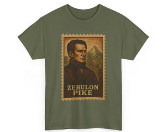 May include: Olive green t-shirt featuring a vintage-style postage stamp design. The stamp depicts a portrait of Zebulon Pike with a mountain landscape background. The text "ZEBULON PIKE" is printed in a serif font at the bottom of the stamp.
