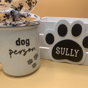 May include: White ceramic mug with the text "dog person" and three paw prints. The mug is in a white wooden crate with a black paw print with the text "SULLY" on it.