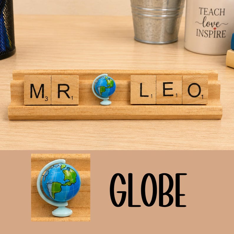 Op de afbeelding: Een houten standaard met lichtbruine vierkante tegels met zwarte letters die MR en LEO spellen, gescheiden door een klein blauw en groen wereldbolfiguurtje. De tegels hebben kleine cijfers in de hoeken en de wereldbol staat op een lichtblauwe voet.